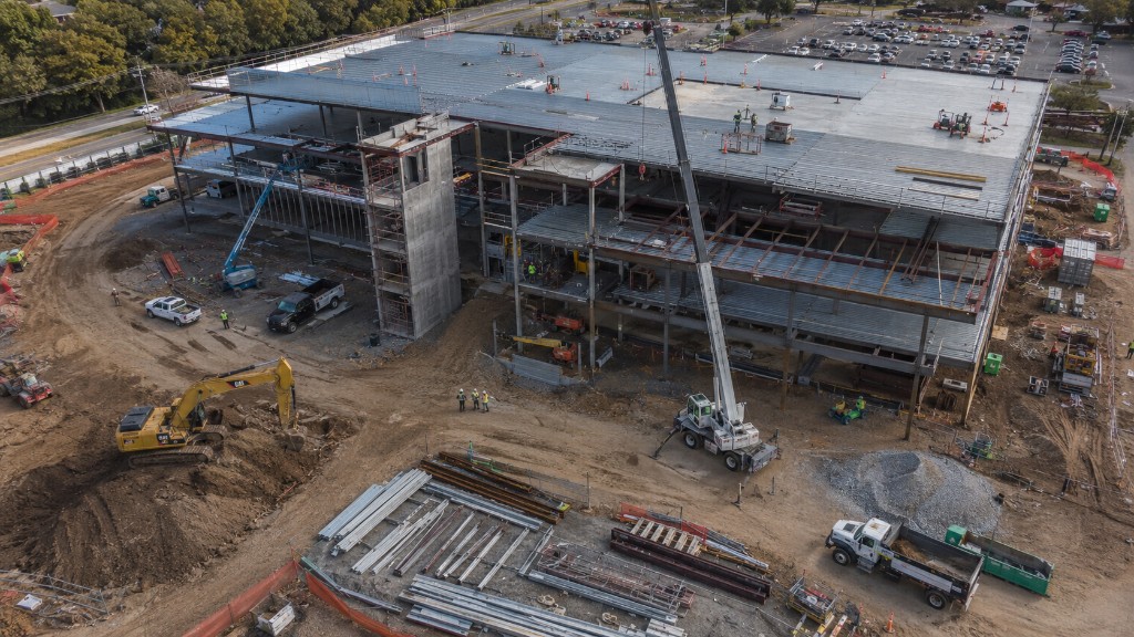 Aerial view of an active commercial construction site with crane, steel frame building, and excavator